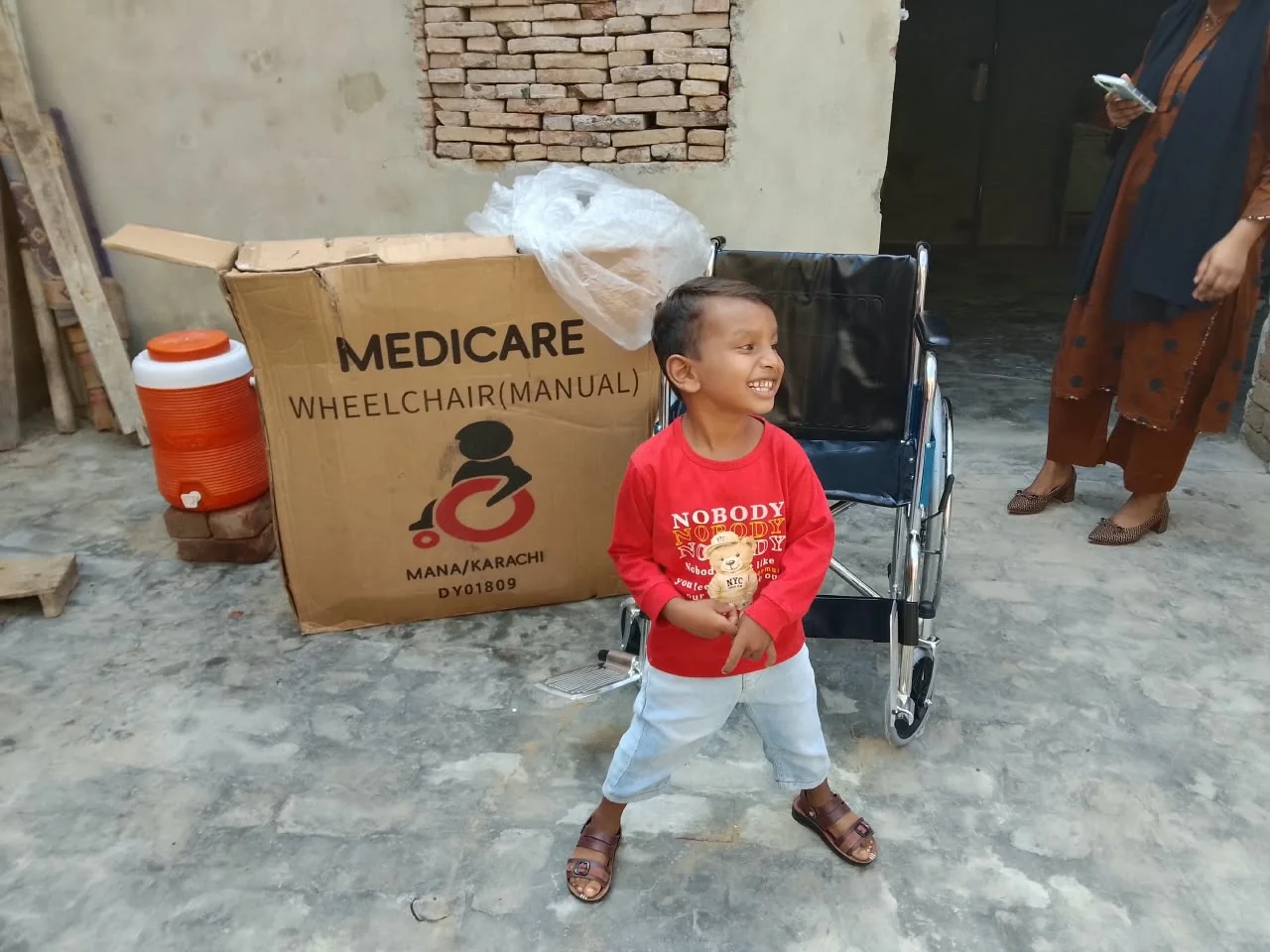 A young community member standing beside a wheelchair